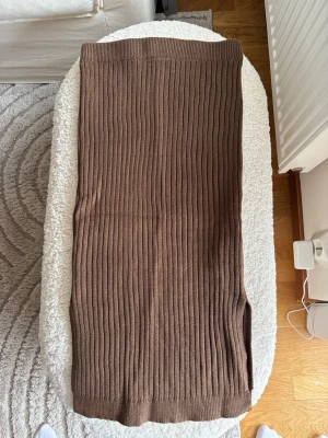 Brun ribbad kjol med slits - Säljer en brun medellång kjol i ribbad stickad kvalitet. Kjolen har en rak passform och en liten slits på sidan för extra rörelsefrihet. Perfekt att styla med en enkel topp eller stickad tröja.