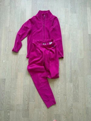 Rosa fleece-set från Polarn O. Pyret - Mysigt rosa fleece-set från Polarn O. Pyret med dragkedja på tröjan och matchande byxor. Perfekt för chill dagar hemma eller som extra lager. Tillverkat i mjuk fleece som håller dig varm och bekväm.