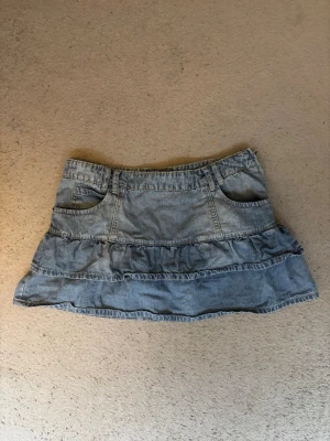 Blå volang jeans kjol - Säljer en blå jeanskjol med volangdetaljer och fickor både fram och bak. Kjolen har en dragkedja på sidan och är ifrån mäket fishbone i storlek L!!