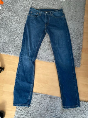 Blå raka jeans från Levi's - Klassiska blå jeans från Levi's med rak passform och fem fickor. Jeansen har en tidlös look med normal midja och Levi's ikoniska läderpatch bak i linningen. Tillverkade i slitstarkt denimtyg som passar perfekt till alla outfits.