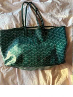 Grön väska  - Snygg grön shoppingväska med klassiskt grafiskt mönster och dubbla långa handtag. Väskan är rymlig och har en mjuk, flexibel form. Perfekt för dig som vill ha en trendig och praktisk väska till vardagen. Har lite repor under