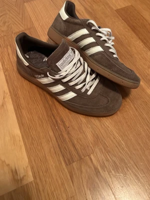 Adidas spezial bruna - Snygga Adidas Samba sneakers i grå mocka med vita detaljer och klassiska tre ränder på sidan. Skorna har vit sula, vita skosnören och en låg profil som ger en clean och tidlös look. Perfekta för dig som gillar streetwear och sportig stil.