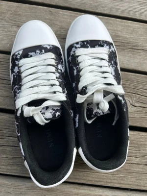 Svarta och vita sneakers med snörning - Säljer ett par snygga sneakers i svart och vitt med coolt mönster och vita snören. Skorna har vit tå och sula samt svart insida. Perfekta för dig som vill ha en unik look till vardagsoutfiten.
