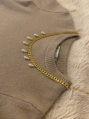 Guldfärgat halsband med pärldroppar - Snyggt halsband i guldfärgad rostfritt med droppformade pärlor som hänger längs kedjan. Perfekt för att ge en trendig touch till din outfit. Halsbandet har en klassisk kedjedesign och pärlorna ger en elegant kontrast.