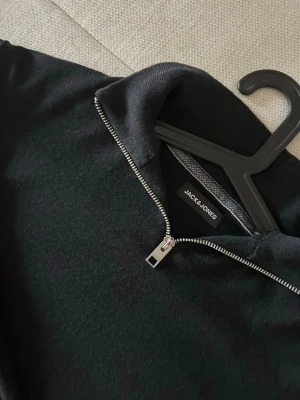 Svart halvzip-tröja Jack & Jones - Stilren svart tröja från Jack & Jones med halv dragkedja vid halsen. Tröjan har ribbade muddar vid ärmslut och nederkant samt en mjuk, tunn stickning som passar perfekt till lager-på-lager. Enkel och snygg design som funkar till det mesta. Skriv för fler frågor!