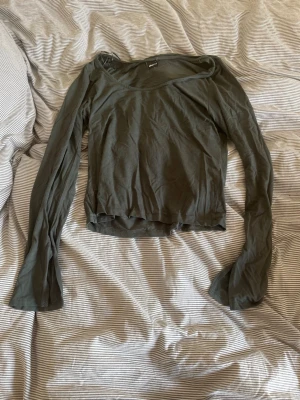 Mörkgrön långärmad croppad topp - Snygg mörkgrön långärmad topp med croppad passform och bred urringning. Tillverkad i mjukt och tunt material som känns skönt mot huden.