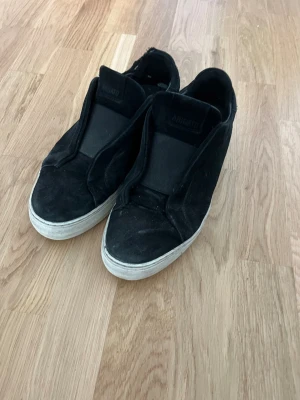 Axel arigato skor - Säljer ett par svarta slip-on sneakers i mocka med vit sula. Skorna har en minimalistisk design utan synliga snören och en låg siluett som passar till många olika stilar. Perfekta för dig som gillar enkel och clean look. Box och dustbag ingår. Priset inte hugget i sten.