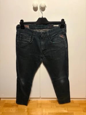 Replay anbass jeans - Säljer ett par jeans med snygga slitningar och kontrastsömmar. Jeansen har fem fickor, knappgylf och en smal passform som sitter tajt vid benen. Perfekta för dig som gillar en modern och stilren look.