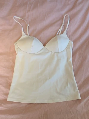 Vit soft shaping singlet topp - Vit linnetopp från Gina Tricot med tunna justerbara axelband och vadderade kupor. Toppen är ärmlös och har en slim passform. Materialet är mjukt och stretchigt för en bekväm känsla.