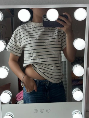 Randig vit t-shirt med svarta ränder - Säljer en klassisk vit t-shirt med svarta horisontella ränder. T-shirten har korta ärmar, rund halsringning och en avslappnad passform. Perfekt till jeans eller shorts för en enkel och stilren look.