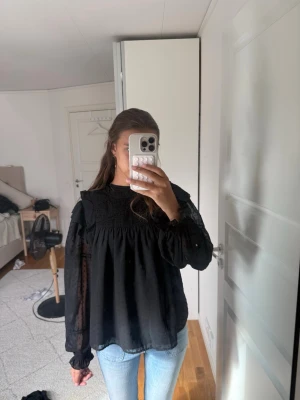 Svart transparent blus med volanger - Säljer en svart blus med transparenta, puffiga ärmar och volangdetaljer. Blusen har smock upptill och små diskreta prickar i tyget. Perfekt för dig som gillar en romantisk och trendig stil. Materialet känns lätt och luftigt.💕