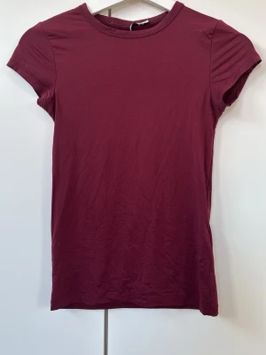Vinröd kortärmad t-shirt - En enkel och stilren vinröd t-shirt med rund hals och korta ärmar. Tillverkad i stretch material som känns skönt mot huden. Använd men har inga stora defekter!
