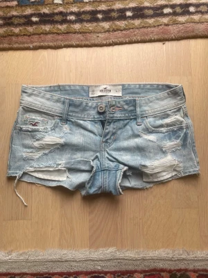 Ljusblå slitna jeansshorts Hollister - Säljer dessa upersnygga jusblå jeansshorts från Hollister med slitna detaljer då de inte passar. Klassisk femficksmodell, knappgylf och bälteshällor. Storlek xxs. Pris är diskuterbart!