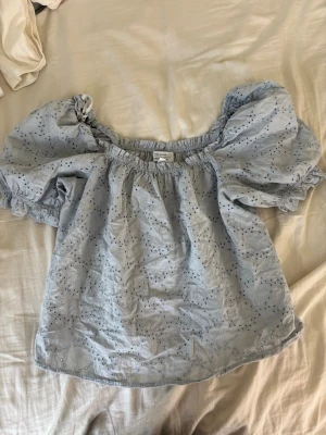 Ljusblå offshoulder blus från & Other Stories - Supersöt ljusblå offshoulder blus från & Other Stories med broderade detaljer och puffiga ärmar. Blusen har resår vid halsringningen och ärmarna, vilket ger en romantisk och trendig look. Perfekt till jeans eller kjol för en fräsch sommarstil.