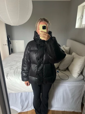 Svart dunjacka hm - Säljer en svart dunjacka med hög krage och dragkedja framtill. Jackan har en oversized passform och elastiska muddar vid ärmsluten. Perfekt för kalla vinterdagar och riktigt skön att bära. Materialet är glansigt och ger en modern look. Väldigt bra skick! Nypris runt 2000