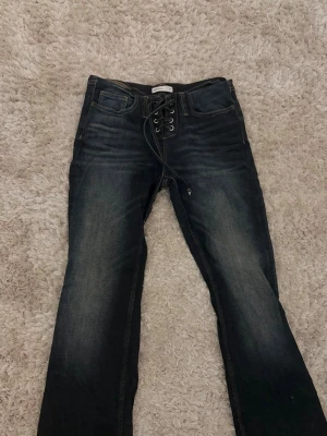 Mörkblå jeans med snörning fram - Säljer ett par lågmidjade mörkblå jeans med snygg snörning framtill. Jeansen har en lätt utsvängd passform