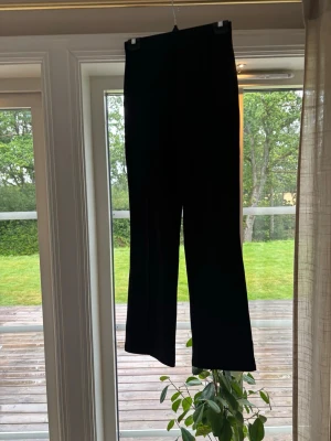 Svarta utsvängda kostymbyxor  - Säljer ett par svarta kostymbyxor med hög midja och utsvängda ben. De har en enkel och stilren design utan synliga detaljer eller fickor. Perfekta för dig som gillar en clean look och vill ha något bekvämt men ändå trendigt.