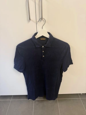 Marinblå linne pikétröja från Stenströms, Stl L - Klassisk marinblå pikétröja från Stenströms med krage och tre knappar framtill. Tillverkad i mjuk bomull som känns skön mot huden. Perfekt till jeans eller shorts för en avslappnad men snygg look.