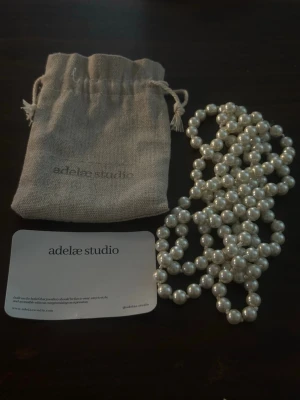 Pärlhalsband från adelae studio - Säljer ett 148 cm långt, elegant halsband med vita pärlor från adelae studio. Halsbandet har klassisk design med runda pärlor och kommer med en snygg tygpåse för förvaring. Perfekt accessoar för att lyfta din outfit. Nypris är 599kr, aldrig använt. Går även att hämta i centrala Kungälv, om det önskas 