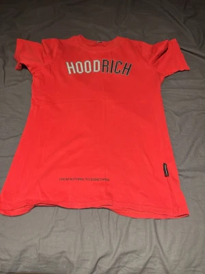 Röd HOODRICH t-shirt med tryck - Snygg röd t-shirt från HOODRICH med stort tryck på bröstet och texten 'FROM NOTHING TO SOMETHING' nedtill. Klassisk passform med rund hals och korta ärmar. Perfekt för en streetwear-look.
