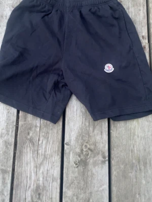 Svarta shorts med Moncler-logga - Svarta shorts från Moncler med elastisk midja och klassisk Moncler-logga på vänster ben. Tillverkade i mjukt material som känns skönt mot huden. Perfekta för sommardagar eller chill hemma.