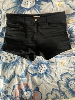 Svarta shorts från H&M, storlek 38 - Snygga svarta shorts från H&M i storlek 38. Klassisk femficksmodell med knapp och dragkedja framtill. Shortsen har uppvikta benslut och är perfekta för varma dagar. Materialet känns mjukt och bekvämt mot huden.