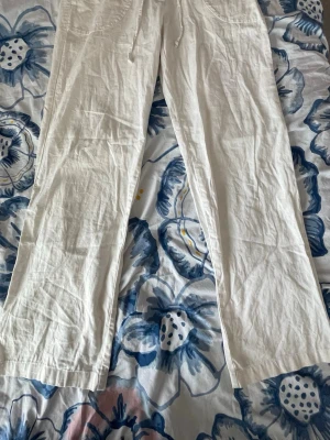Vita linnebyxor med dragsko - Säljer ett par vita linnebyxor med raka ben och avslappnad passform. Byxorna har dragsko i midjan och stora fickor framtill. Perfekta för en chill och stilren look under varma dagar.