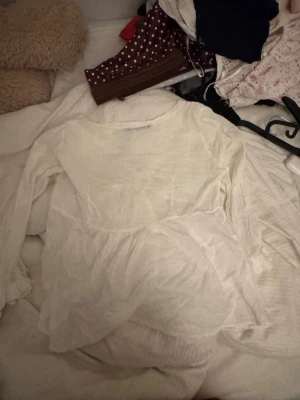 Vit långärmad topp med spets - Söt vit topp med lång ärm och fina spetsdetaljer vid halsen. Toppen har en lätt volang nedtill och är tillverkad i ett tunt, luftigt tyg. Perfekt för sommarens alla tillfällen och ger en romantisk vibe.