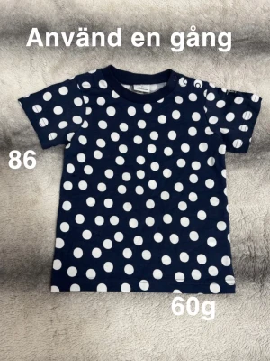 Mörkblå prickig t-shirt barn - Mörkblå t-shirt med vita prickar i ett lekfullt mönster. Klassisk rund halsringning och korta ärmar. Perfekt för dig som gillar färg och mönster i vardagen.🌸Använd en gång. Storlek 86