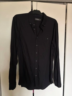 Svart slim fit skjorta Dressmann - Stilren svart skjorta från Dressmann i slim fit-modell. Skjortan har långa ärmar, klassisk krage och knäppning framtill. 
