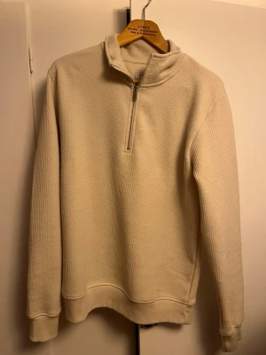 Vit halvzip hoodie från Primark - Säljer en beige hoodie från Primark i storlek S. Tröjan har halv dragkedja framtill, ribbade muddar och en mjuk, strukturerad yta. Perfekt för dig som gillar enkel och clean stil. Materialet känns skönt mot huden och passar till många olika outfits.