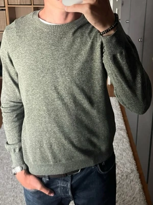 Oscar Jacobson stickad tröja i olivgrönt - stl M - Oscar Jacobson stickad tröja i olivgrönt, storlek M. 100% bomull, tunn stickning med slät yta. Rak passform, funkar över till mycket, både nu och i höst. Personen på bilden är 189cm, väger 78kg.   Använd men i mycket fint skick, inga hål eller fläckar.  Rök- och djurfritt hem. Skriv gärna om du vill ha fler bilder eller undrar något!