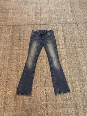 Blå bootcut jeans med slitningar - Snygga blå bootcut jeans med lätt slitna detaljer framtill. Klassisk knappficksmodell och normal passform. 