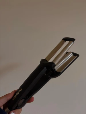 BaByliss vågtång för hårstyling - BaByliss vågtång med svart handtag och guldfärgade värmeplattor. Perfekt för att skapa snygga vågor i håret. Ergonomisk design med tre cylindrar i metall och plastdetaljer. Enkel att använda för att fixa frisyren snabbt.