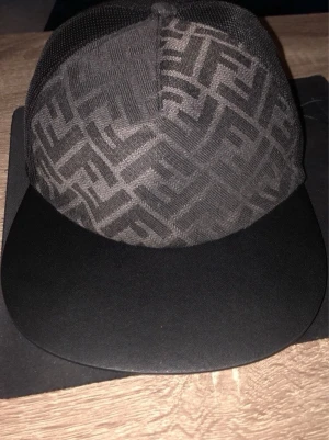  Fendi keps  - Säljer en svart keps fran Fendi med det klassiska FF-logomönstret över hela kepsen. Kepsen har böjd skärm och justerbar rem baktill med Fendi Roma-detalj.Köpte fel variant därför säljer den 