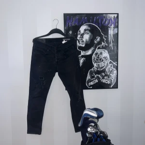 Svarta slim jeans från dondup - Svarta slim jeans från George med slitningar och färgstänk för en edgy look. Klassisk femficksmodell med dragkedja och knapp. Jeansen har smal passform och är tillverkade i stretchigt denim för extra komfort.