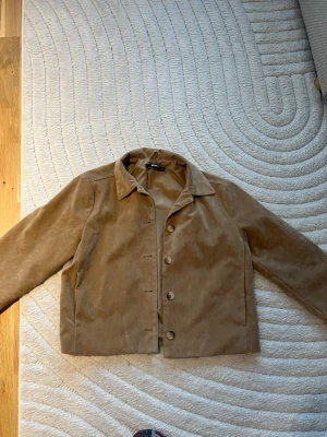 Beige mocka från Gina Tricot - Snygg beige mocka från Gina Tricot i storlek XS. Jackan har klassisk krage, raka ärmar och knäppning framtill. 