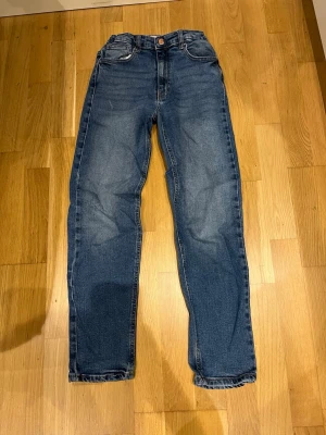 Blå raka jeans från only - Säljer ett par klassiska blå jeans med rak passform och hög midja. Jeansen har fem fickor, knappgylf och subtila slitningar för en avslappnad look. Perfekta till vardags och passar till det mesta i garderoben.