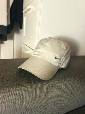 Vit Keps NIKE Dri-Fit - En stilren keps från Nike. Denna keps är gjord av lätt och mjuk polyester, med fukttransporterande Dri-FIT-teknik. Kepsen har ett justerbart metallspänne baktill som gör det enkelt att justera passformen. Ett snyggt val för soliga dagar.