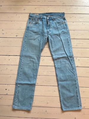 Ljusblå raka jeans Levis 501 - Säljer ett par klassiska ljusblå jeans med rak passform och fem fickor. Jeansen har hög midja och är tillverkade i kraftig denim. Perfekta för en avslappnad och tidlös stil. Modell Levis 501