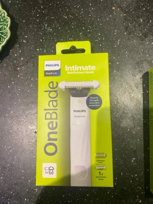 Philips OneBlade Intimate blad - Philips OneBlade Intimate SkinProtect-blad i limegrön och vit förpackning. Innehåller ett rakblad och en trimmerkam, speciellt utformad för intimrakning med extra hudskydd. Enkel att använda och smidig att ta med.