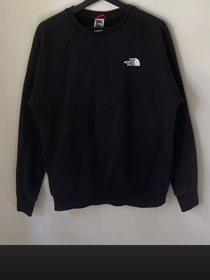 Svart sweatshirt från The North Face - Svart sweatshirt från The North Face med liten logga på bröstet och stor logga samt texten 'Never Stop Exploring' på ryggen. Klassisk rund halsringning och ribbade muddar vid ärmslut och nederkant. Perfekt för en avslappnad och stilren look.