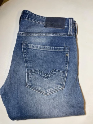 Blå raka jeans från Replay - Snygga blå jeans från Replay med raka ben och klassisk femficksmodell. Jeansen har slitningar och tvättade detaljer för en avslappnad look. Tillverkade i denim med en skön passform och Replay-logga på bakfickan.