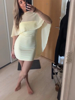 Gul klänning - Trendig ljusgul kort klänning från Gina Tricot med cape-detalj som ger en unik och flowy look. Klänningen är ärmlös och har en kroppsnära passform. Perfekt för dig som vill sticka ut med en modern och stilren outfit.