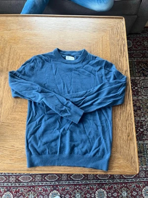 Blå marinoul tröja med rund hals - Mysig blå marinoul tröja med rund hals och långa ärmar. Tröjan har ribbade muddar vid ärmslut och nederkant. Perfekt för lager på lager och enkel att matcha med jeans eller kjol.