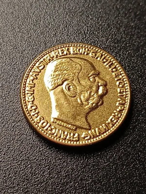 Österrikisk 20 Corona guldmynt 1915 vikt: ca 6,1g - Säljer en österrikisk 20 Corona guldmynt från 1915. Myntet är gyllene och har ett porträtt av kejsare Franz Joseph I på ena sidan och en dubbelörnsymbol på andra sidan. Perfekt för samlare av mynt eller historiska föremål. Vikt: ca 6,1g och diameter: nästan ca 21mm. Myntet är nog gjort av koppar eller mässing med guldplätering eller liknande och myntet är inte magnetiskt så de är ett fint mynt för samlare. Väldigt realistisk och likt ett äkta restrike guldmynt.