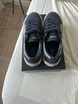 Mörkblå Dior B33 - Snygga mörkblå sneakers från Dior med klassiskt monogrammönster på sidorna och vita sulor. Skorna har tjocka matchande skosnören och låg profil. Perfekta för dig som vill ha en exklusiv och trendig look.