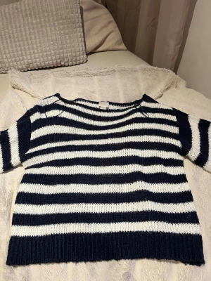 Marinblå och vit randig stickad tröja - Stickad tröja med breda marinblå och vita ränder. Tröjan har rund halsringning, ribbstickade muddar och avslut. Materialet ser ut att vara mjukt och lite tjockare garn, perfekt för kyligare dagar. Avslappnad passform och klassisk look.