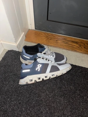 Grå/blå On löparskor sneakers - Snygga sneakers från On i grått och blått med vita detaljer. Ovandelen är i mesh för bra ventilation och sulan har On's unika CloudTec-design för extra komfort. Skorna har vita snören och reflekterande detaljer på sidan.