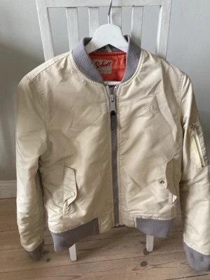 Schott NYC x American College Bomber Jacket Beige / MA-1 Flight size M - .Klassisk och snygg bomberjacka från Schott NYC i samarbete med American College! Ljusbeige/off-white utsida med oranget innerfoder. Den är lite kortare modell vilket gör att den passar med alla underdelar! Mått tas på begäran, pris går att disskutera⭐️ paketpris går att fixa.